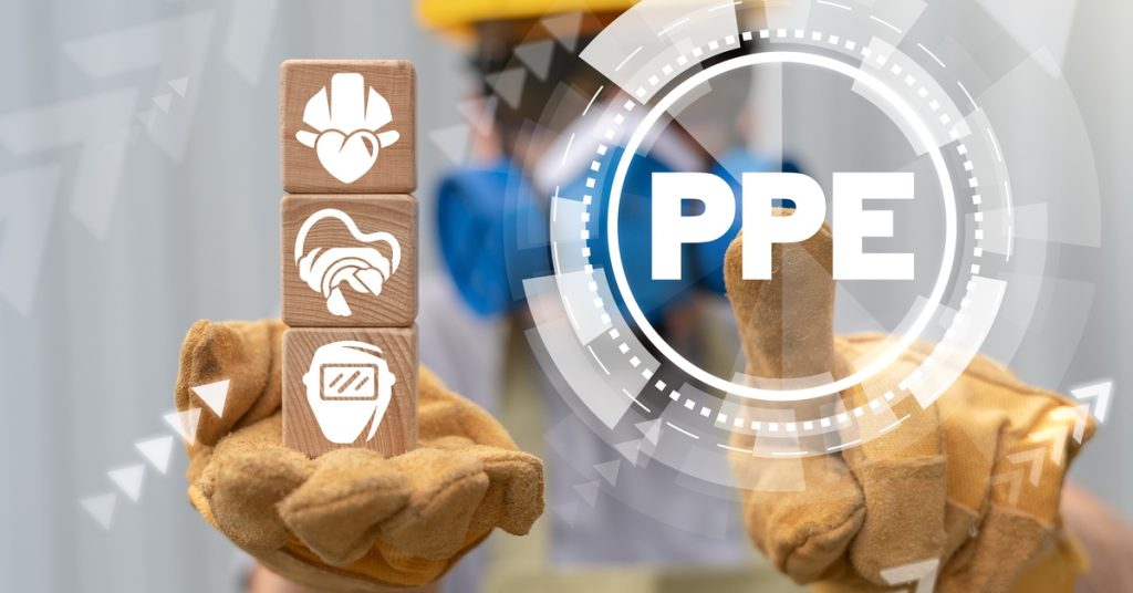 A person wearing gloves, a mask, googles, and a helmet interacts with a graphic that says "PPE" and wooden blocks with PPE item illustrations.