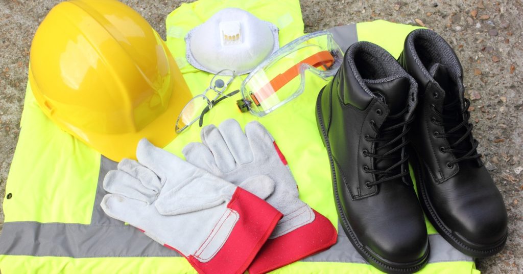 A close up of some personal protective equipment (PPE) stacked on each other, such as boots, hard hats, and goggles.