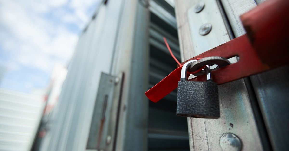 A close-up of a large storage container with the door open and a small padlock attached to a red handle.