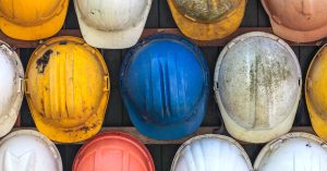 Many hard hats are lined up next to each other, each with a different color and varying levels of dirt on it.