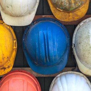 Many hard hats are lined up next to each other, each with a different color and varying levels of dirt on it.