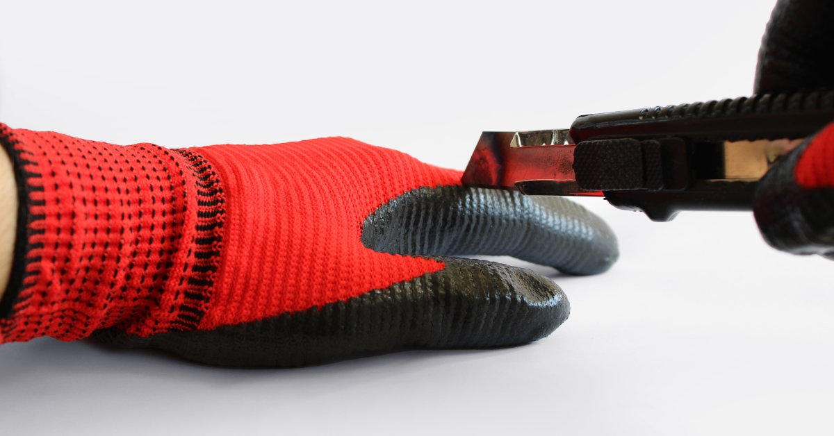 A close-up of someone trying to cut cut-resistant gloves with a utility knife. The gloves are red and black.