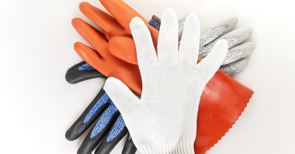A pile of different-colored cut-resistant gloves on top of each other. The gloves lie on a white table.