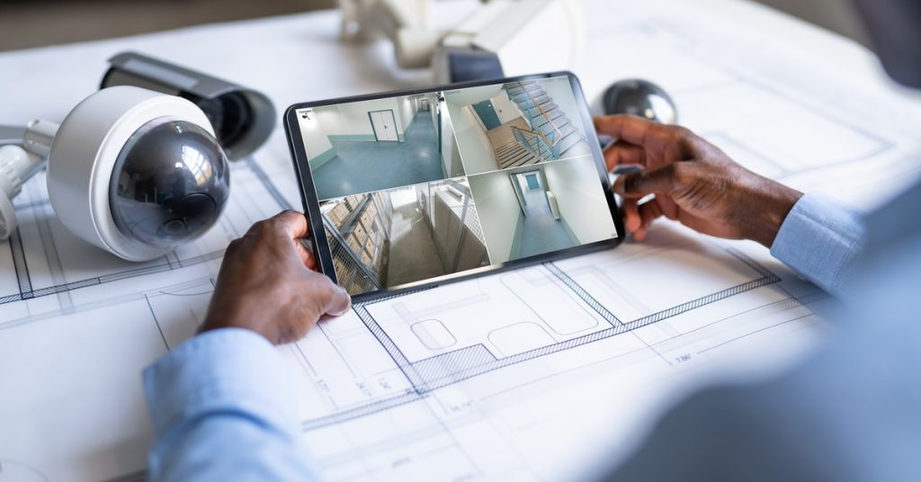 A close-up of someone monitoring business security cameras through a tablet. The person sits near security cameras.