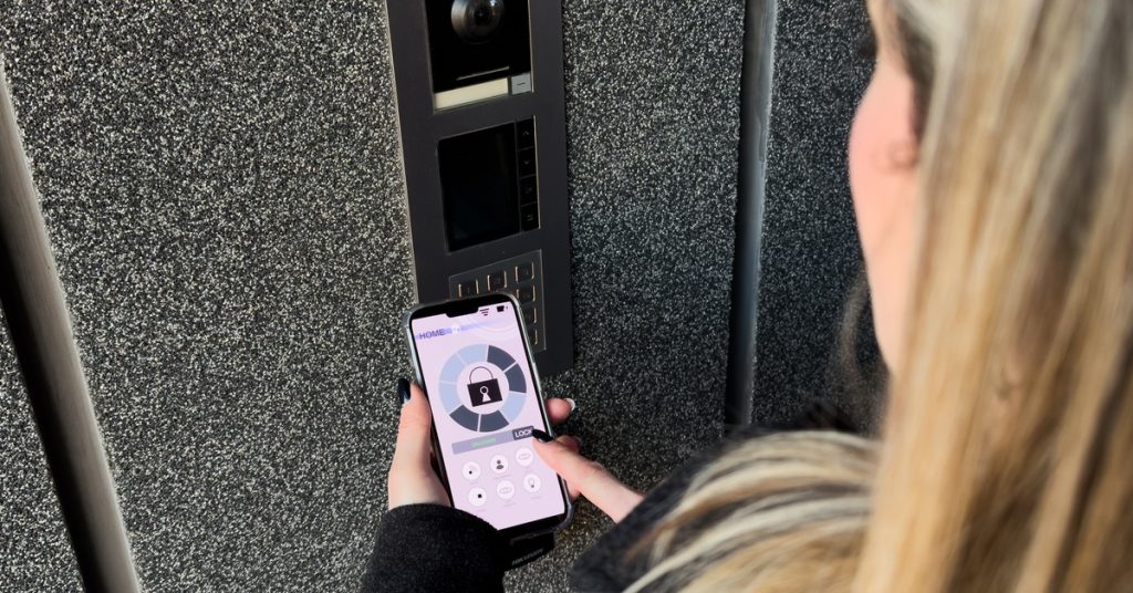 A woman holds a phone with a lock and security-related infographics. She's near a keyless security system.