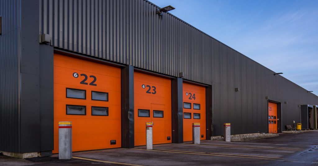 The outside of a large black warehouse building with multiple orange garage doors with numbers on them.