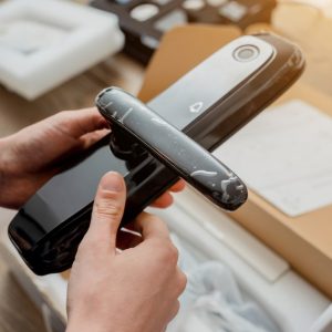Someone holds a keyless door lock with the lock's packaging on the table below. Other packaging components lay on the side.