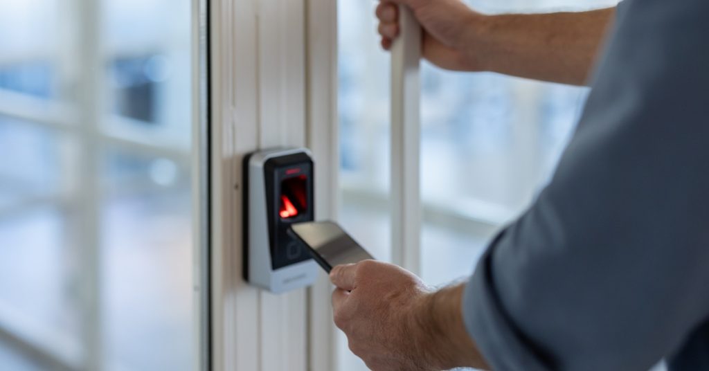 A close-up of a person using their smartphone to unlock a keyless security system. The person also touches the door handle.