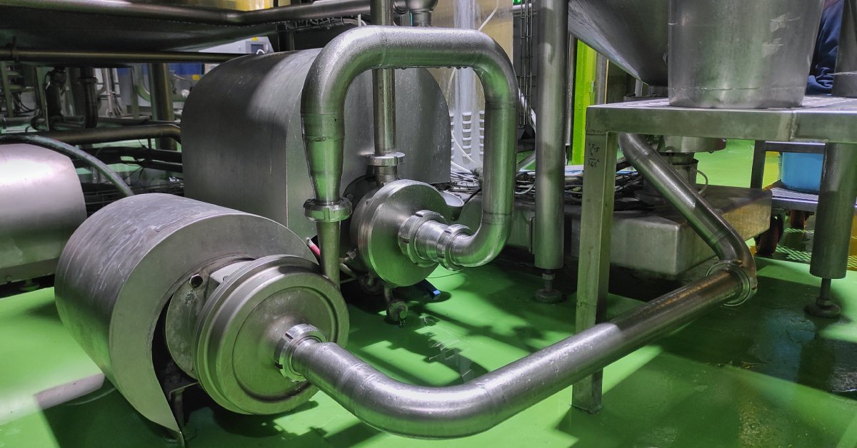 A stainless-steel pipe in a building with a green floor allows the transfer of liquids from one area of the facility to another.