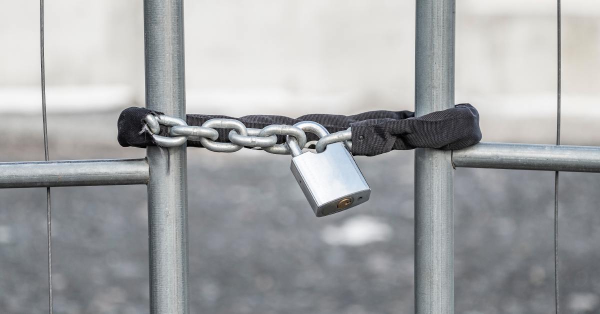 A close-up of a chain with a black fabric over it holding a gate together. A padlock secures the chain and gate.