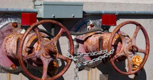 Two shut-off valves outside a building. The valves are very worn down, with a chain and padlock securing them.
