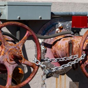 Two shut-off valves outside a building. The valves are very worn down, with a chain and padlock securing them.