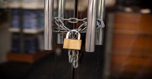 A glass door secured with a metal chain wrapped around two stainless handles and fastened with a brass padlock, preventing entry.