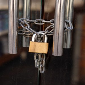 A glass door secured with a metal chain wrapped around two stainless handles and fastened with a brass padlock, preventing entry.