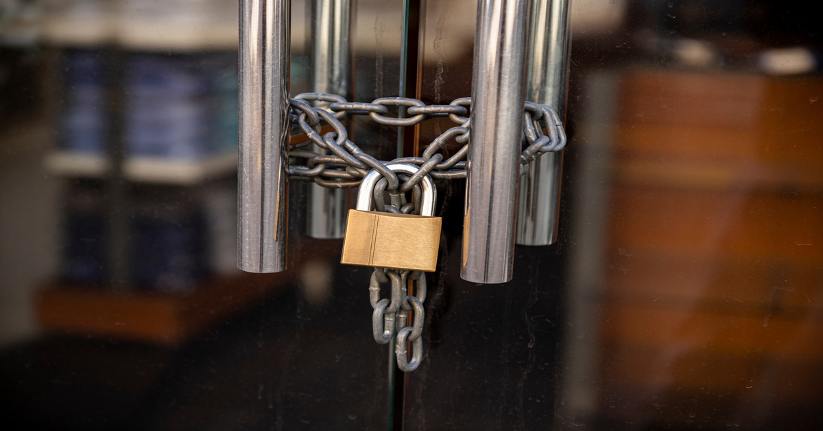 A glass door secured with a metal chain wrapped around two stainless handles and fastened with a brass padlock, preventing entry.