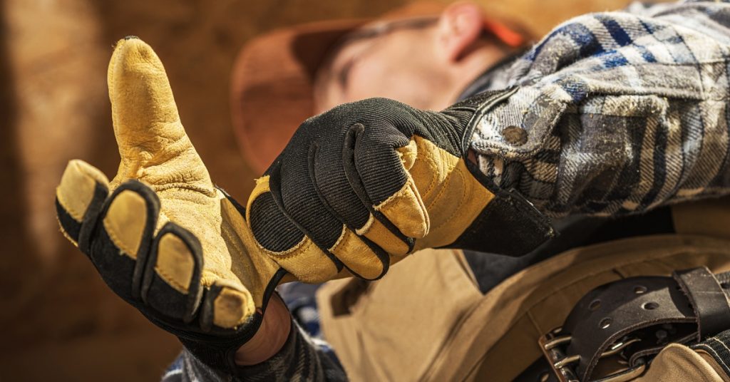 A professional construction contractor wears yellow leather impact gloves with black knuckle padding while at work.