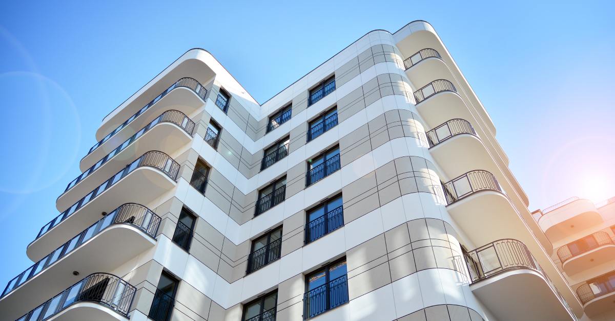 A modern apartment building with a curved white facade and rounded balconies, with a sunny blue sky in the background.