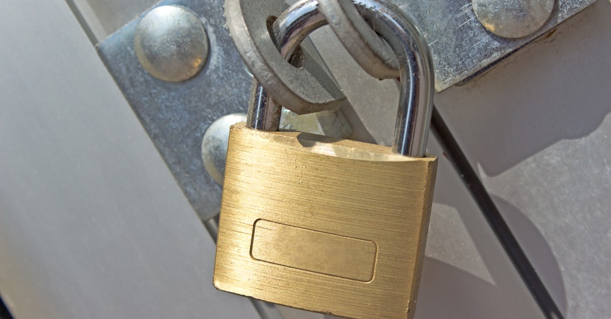 A brass padlock securing a metal latch on an industrial door, highlighting commercial-grade security hardware.