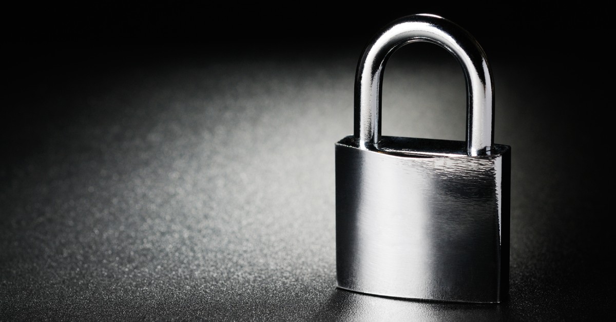 A chrome padlock with a hardened steel shackle on a dark surface, representing commercial security and durability.