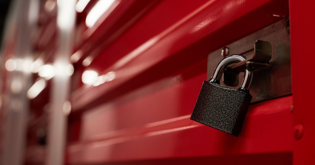 Close-up of a black padlock securing a metal latch on a red corrugated storage unit door, with a blurred background.