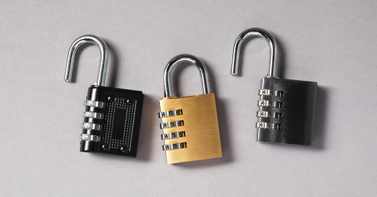 Three open combination padlocks in black, gold, and dark silver arranged on a light gray surface.