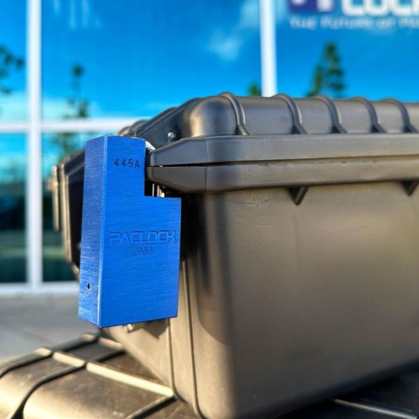 A thick, blue Paclock USA locking mechanism attached to the side of a black container next to some large windows.