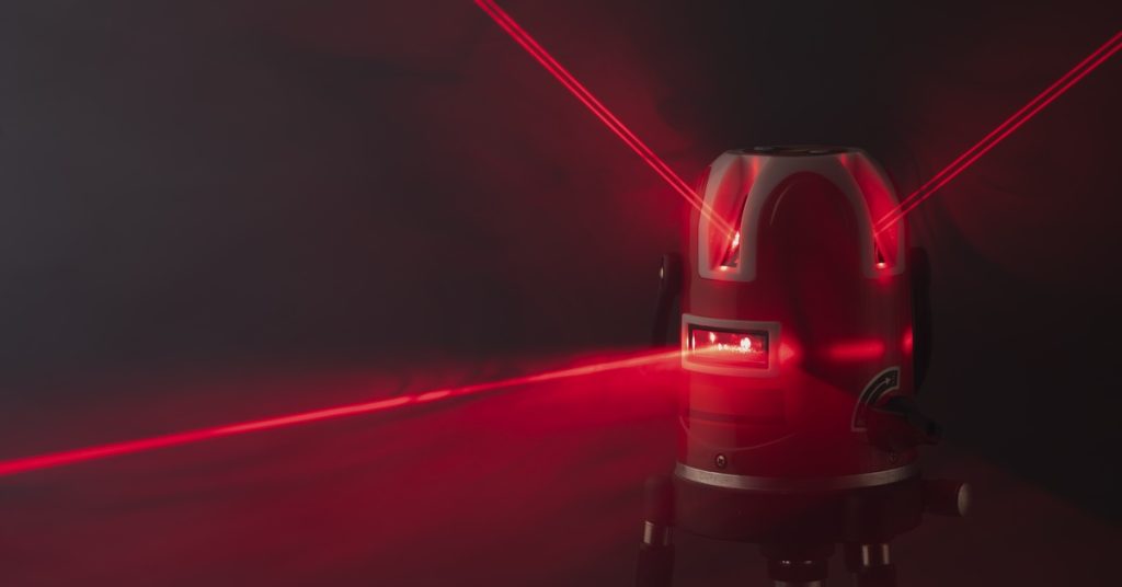 A red self-leveling laser level projecting multiple bright red beams outward against a dark studio background.