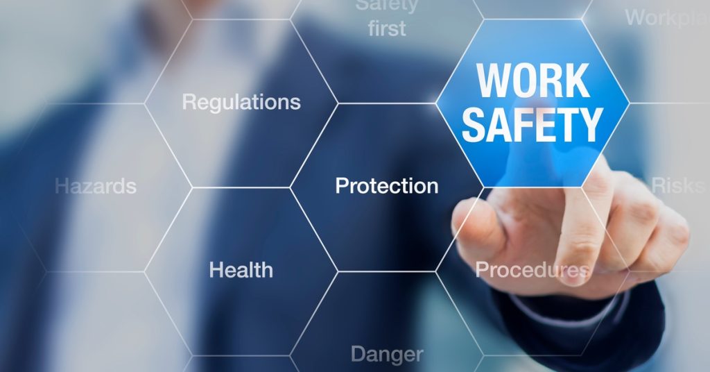 A person presses a work safety icon on a digital screen with protection, regulations, hazards, and risks nearby.