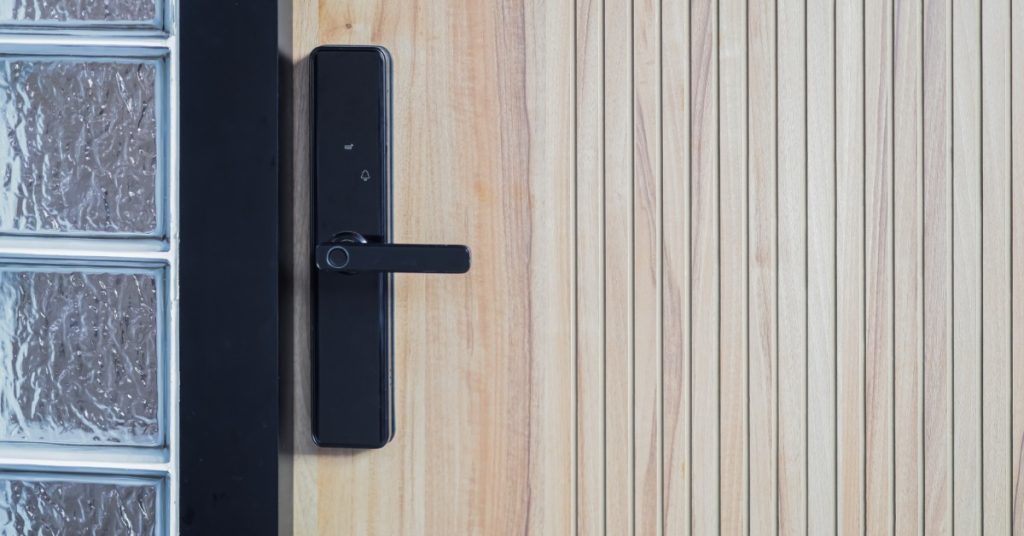 A black smart door lock with a fingerprint scanner and a lever handle on a light wood-slatted door.